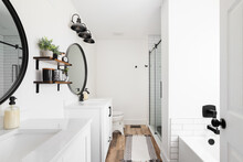 A Modern Farmhouse Bathroom With A White Vanity And Marble Countertop, Circular Black Mirrors, And A View To The White Subway Tile Shower.