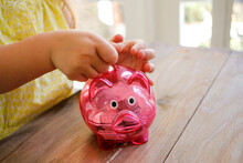 Girl Wearing Yellow Blouse Putting A Coin In A Pink Transparent Piggy Bank