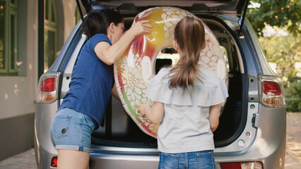 Wall Mural - Woman and little girl loading vehicle with luggage while getting ready for vacation citybreak. Mother and daughter putting luggage in car trunk while enjoying holiday field trip.