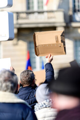 Rear view of senior man holding blank placard carton piece protesting in front of the building - hundreds of people gathered to protest against