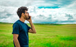 Man on the road talking on the phone, person in the field calling on the phone, young man talking on the phone in the field looking to the side. Handsome man calling on the phone in the field