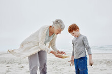 Grandmother And Grandson Standing On Beach Looking At Seashell