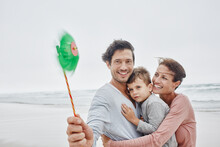 Happy Family Standing On Windy Beach Holding Green Oinwheel