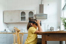 Girl Wearing VR Glasses Sitting At Table In Kitchen