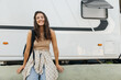 Happy caucasian young lady smiling broadly looking at camera standing by van with house. Brunette wears casual light-colored clothes. Lifestyle concept