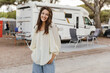 Attractive young caucasian woman looks at camera, spends her weekend camping. Brunette wears casual blouse and jeans. Leisure lifestyle and beauty concept.