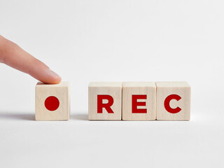 Finger presses the REC record button with the word rec on wooden cubes.