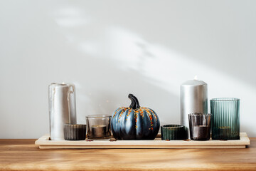 Autumn, fall cozy composition. Gray pumpkin with sequins and burning candles on the wooden tray on the table with white wall background. Scandinavian minimalist hygge home decor. Selective focus