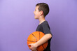 Little boy playing basketball isolated on purple background laughing in lateral position