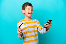 Little Boy Isolated On Blue Background Buying With The Mobile With A Credit Card