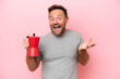 Middle age caucasian man holding coffee pot isolated on pink background with shocked facial expression