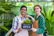 Team of diversity garden worker holding opening sign to welcome customer to their tropical nursery plant center full of exotic fern species