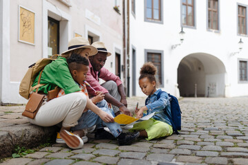 Canvas Print - Multiracial family travel together with suitcases, sitting on ground and looking at the paper map.