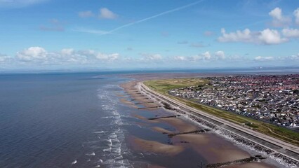 Wall Mural - Aerial view of waves crashing onto the coast with views of buildings and houses in the distance. Taken in Cleveleys Lancashire England. 