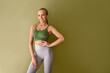 © Velista production - Young attractive sporty woman wearing green top and gray leggings standing near green background and smiling.