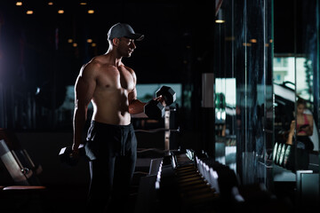 Wall Mural - muscular man working out with dumbbells in gym dark tone,