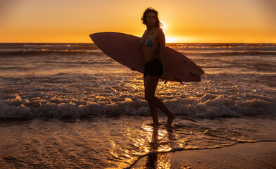 Wall Mural - Woman with surfboard walking near sea at sunset