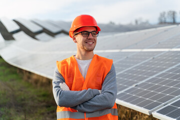 Professional man engineer in orange uniform is posing at the photo camera near the at energy farm