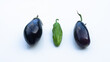 two organic eggplants and a green pepper on white surface