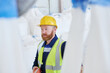 © pressmaster - Bearded male worker in uniform and hardhat pressing buttons on remote control switch while lifting huge heavy sacks with raw materials
