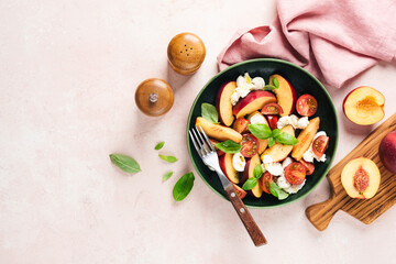 Wall Mural - Salad with peach, mozzarella cheese and tomatoes on green plate, pink background with copy space. Top view. Healthy vegetarian summer fruit and cheese salad