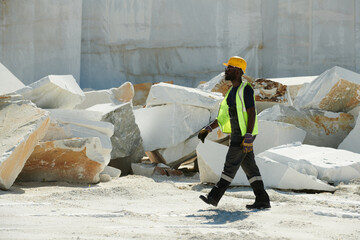 Aufkleber - Young African American male engineer in workwear and hardhat hurrying to workplace while moving along thick rock wall of factory