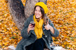 Portrait of a beautiful woman in a gray coat and a yellow beret with a scarf sitting under a tree holding tea and smiling. Space for text. Unity with nature, mental health