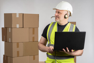 Poster - Online store employee. Man with laptop to and headphones dispatcher. Online store manager near boxes. E-commerce dispatcher career. Warehouse worker in white helmet. Warehouse manager on dispatcher