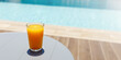 Glass of fresh cool orange juice drink on table next to swimming pool , summer tropical holiday concept. Banner with copy space