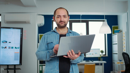 Poster - portrait of casual business man holding laptop typing on keyboard and smiling at camera in busy mode