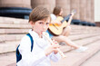  a boy plays a wind instrument on the steps of a music school outside.