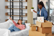 © Syda Productions - moving, people and real estate concept - happy smiling woman unpacking box and her friend resting on sofa at new home