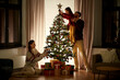 © Syda Productions - family, winter holidays and people concept - happy mother, father and little daughter decorating christmas tree at home