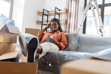 Sticker - moving, people and real estate concept - happy smiling woman with boxes sitting on sofa with cup of coffee at new home