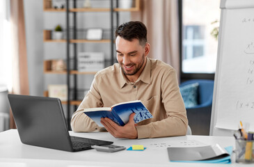 Canvas Print - distant education, school and remote job concept - happy smiling male math teacher with laptop computer, book and flip chart having online class or video call at home office