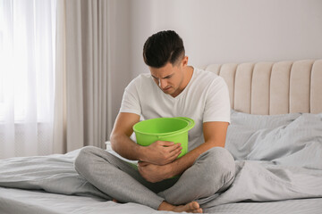 Poster - Man with bucket suffering from nausea on bed at home. Food poisoning