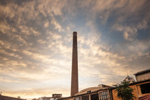 Selective Blur On Broken Red Brick Chimney From An Abandoned Factory At Dusk, With Sun, Dating Back From The Industrial Revolution In A Bankrupted Industry.....