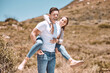 Happy and in love couple having fun in nature and enjoying quality time together. Cute and relax boyfriend piggyback or carrying girlfriend with a smile on a bonding and romantic countryside date