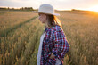 © olga_sova - A beautiful middle-aged farmer woman in a straw hat and a plaid shirt stands in a field of golden ripening wheat during the daytime in the sunlight