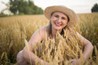 © olga_sova - A beautiful middle-aged farmer woman in a straw hat and a plaid shirt stands in a field of golden ripening wheat during the daytime in the sunlight