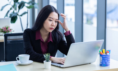 Upset thoughtful Young Asian business woman stress in the workplace working with laptop computer of Office staff are not happy in with working colleagues behind in the office