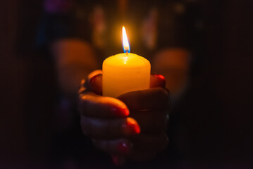 Wall Mural - Candle in female hands on black dark background.Prayers candle in hands.