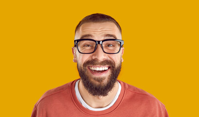 Poster - Studio portrait of happy man in glasses. Closeup headshot of cheerful funny bearded nerdy young man wearing eyeglasses looking at camera, smiling and laughing isolated on yellow orange background