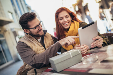 Wall Mural - Happy young couple using a digital tablet together at a coffee shop.