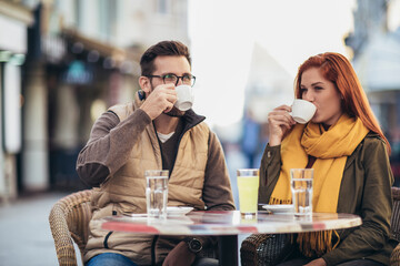 Wall Mural - Attractive young couple in love sitting at the cafe table outdoors, drinking coffee