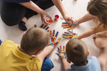 teacher works with children according to the Montessori method and paints their hands. Kindergarten teacher therapy session with children with autism spectrum disorder.