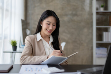 Wall Mural - Beautiful Asian woman sitting in the office using a laptop .Happy business woman smiling and enjoying work.