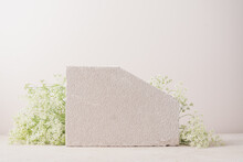 Minimal Concrete Background For Branding And Packaging Presentation. Textured Stone On A Beige Background With White Flowers