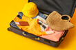 Suitcase with clothes, beach accessories, ticket and passport on yellow background
