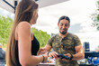© PoppyPix - Unconventional hobby concept. Long-haired young caucasian woman buying a gun from gun reseller. Handsome dark-hair caucasian man with a goatee showing a pistol to his female client. High quality photo
